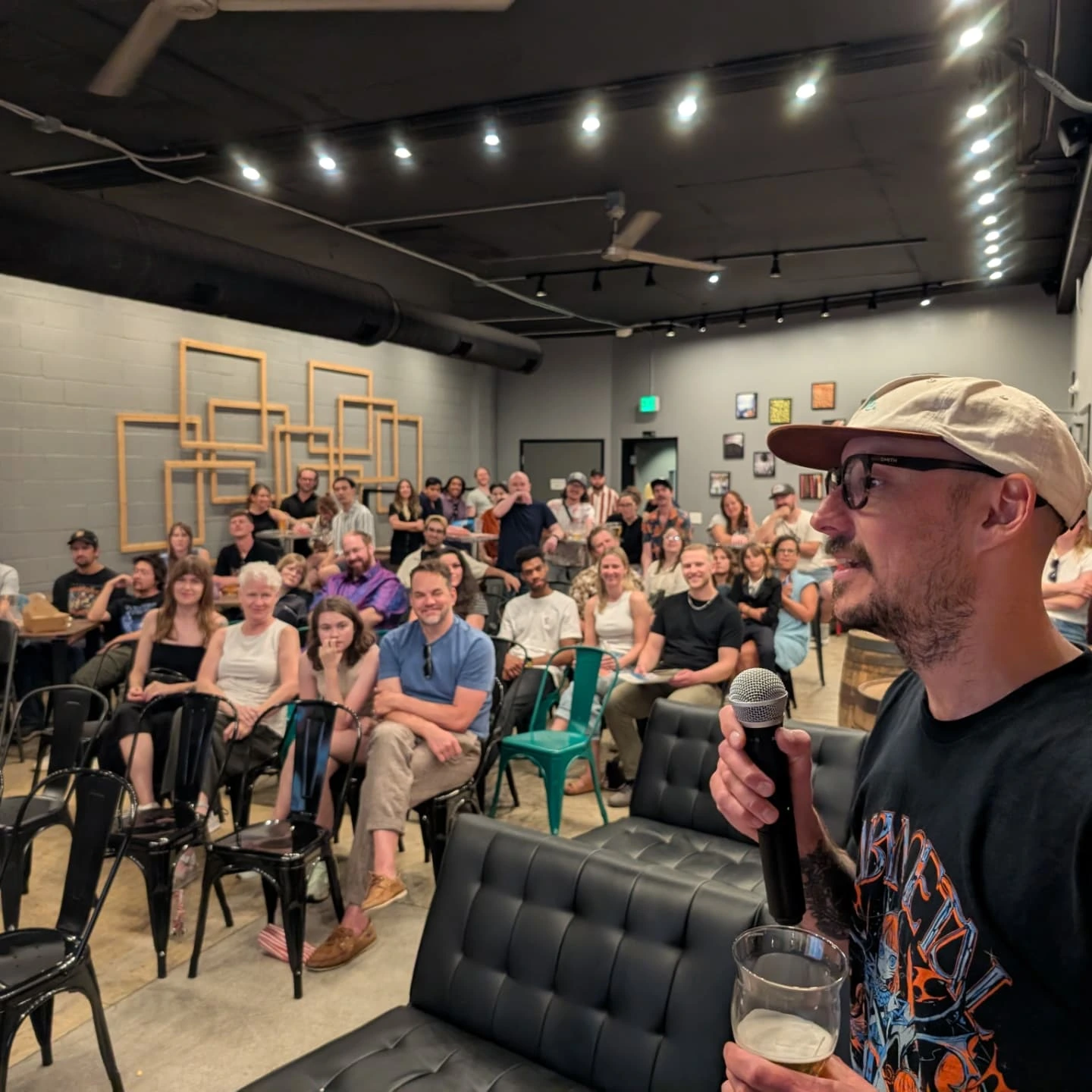 Side Hustle Film Fest co-founder CJ Coccia holding a microphone in front of an audience at River North Brewery, RiNo